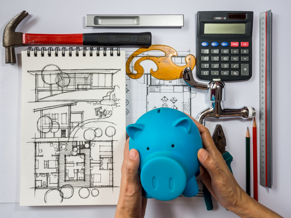 hand holding piggy bank, house plans, tools, calculator
